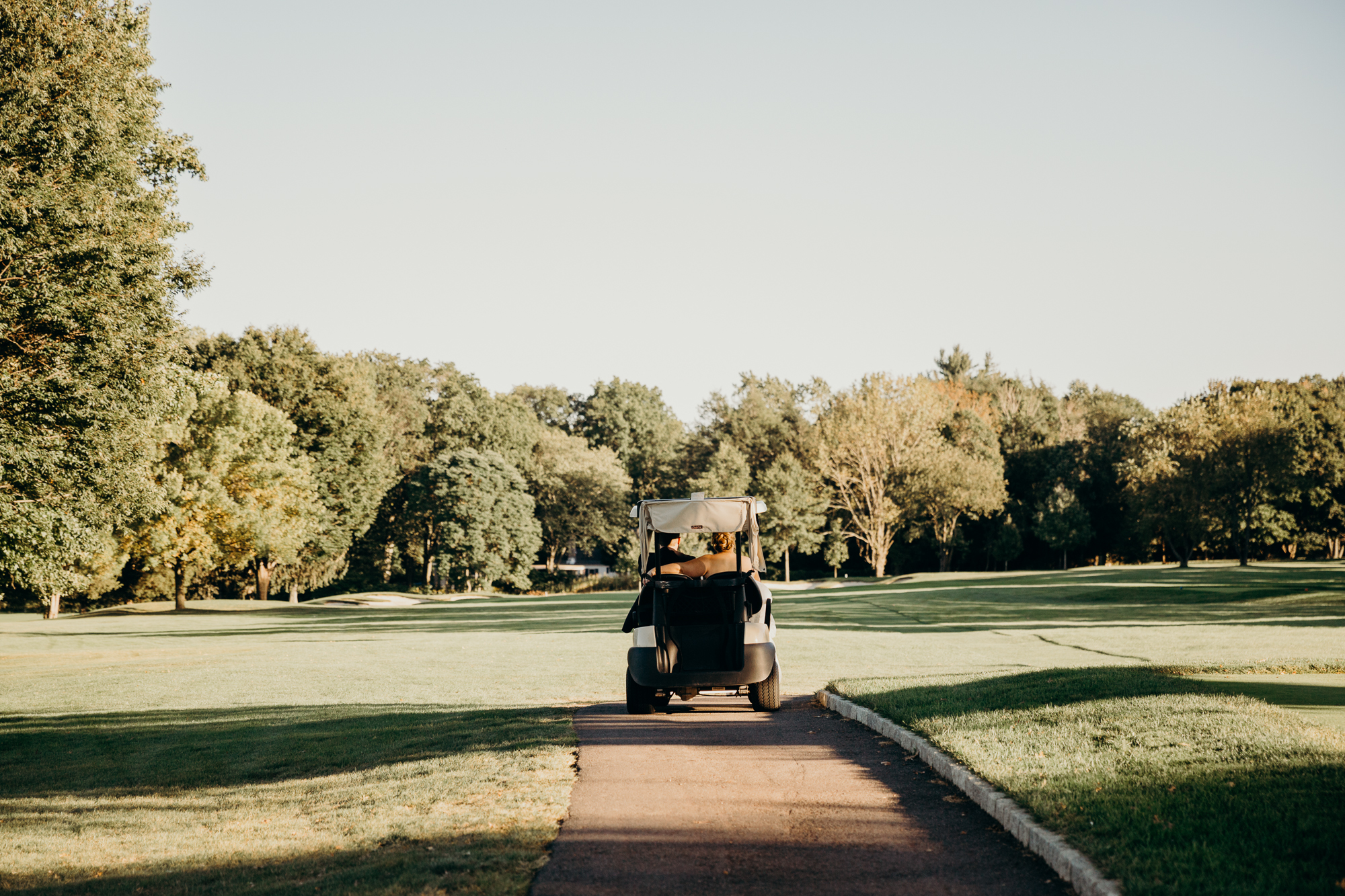 bride and groom ride away on a golf cart at country club of darien in darien, connecticut