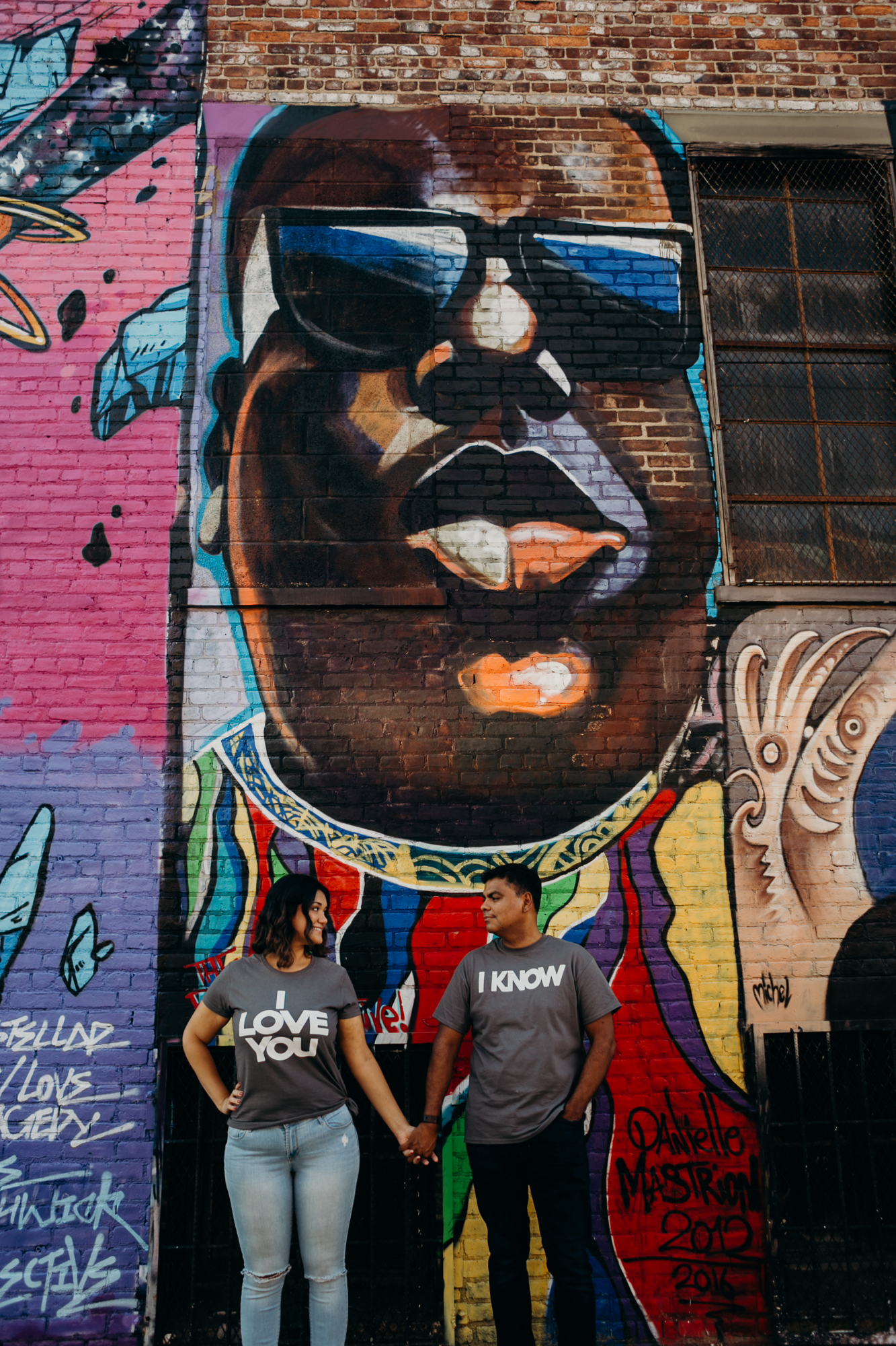 a couple stands in front of a mural in bushwick, brooklyn