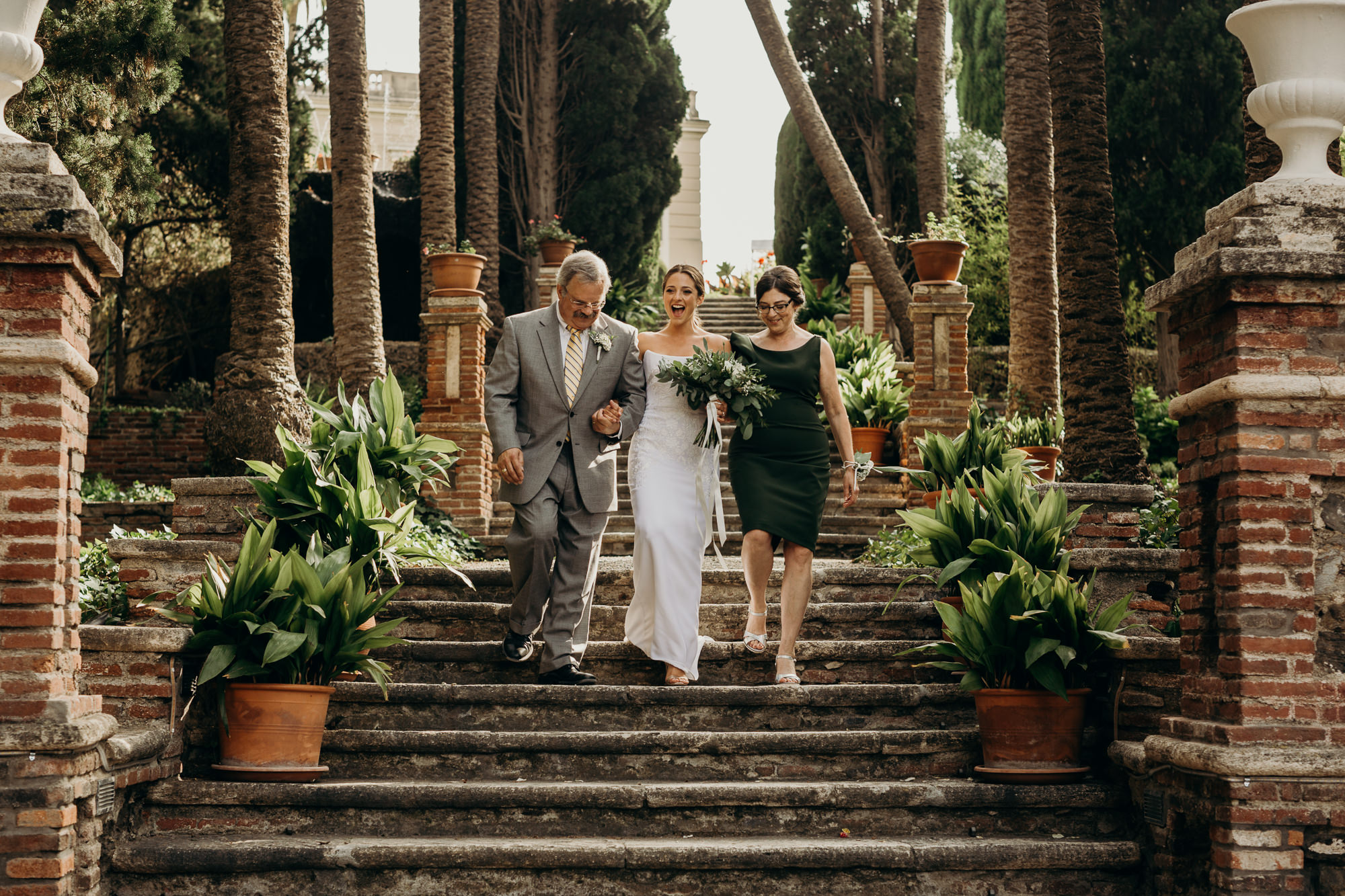 a bride walks down a staircase with her parents to her wedding at casa de los bates in nerja, spain