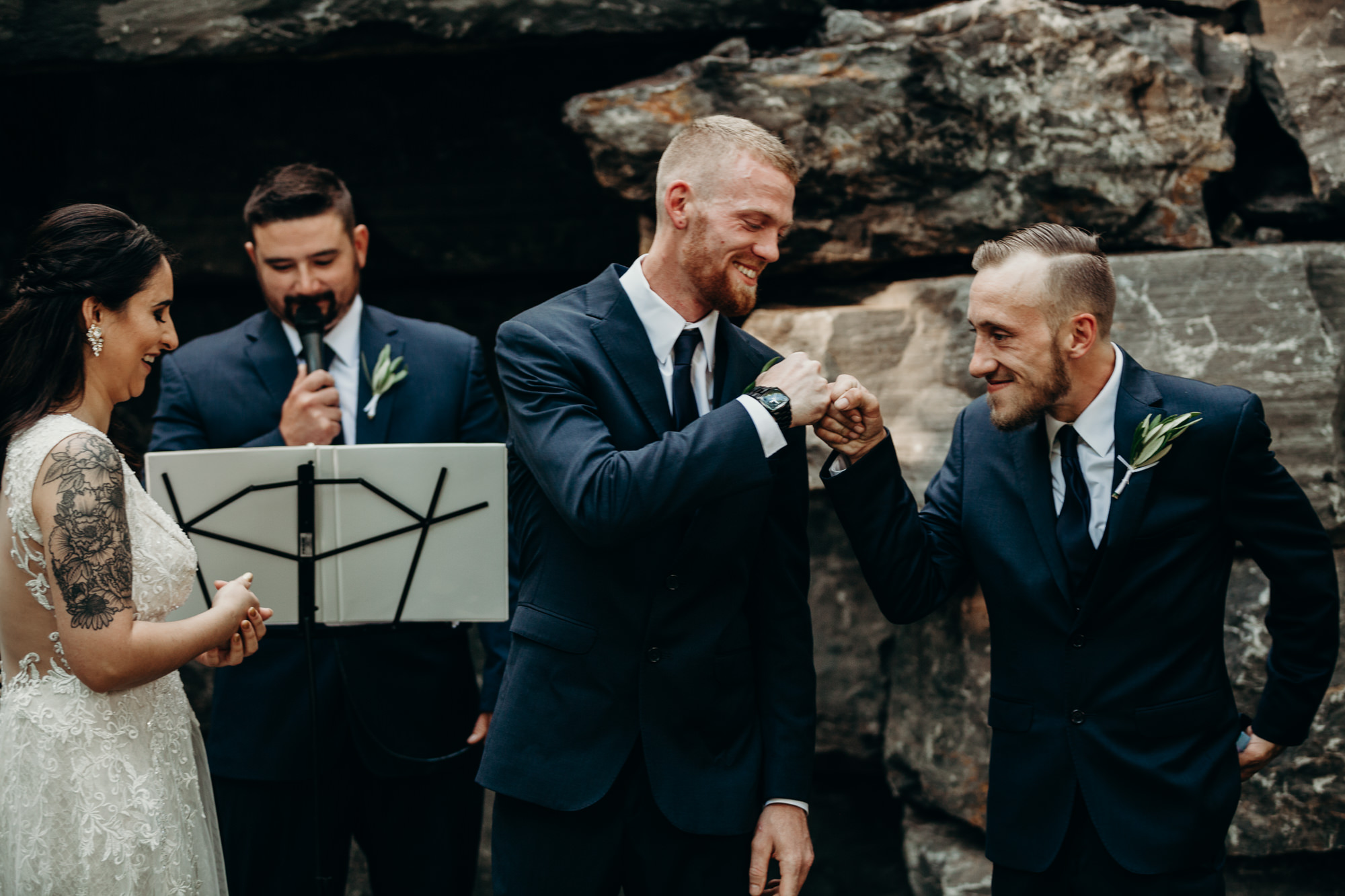 a groom and his best man pound fists at the wedding ceremony at the dibbles inn in syracuse, ny