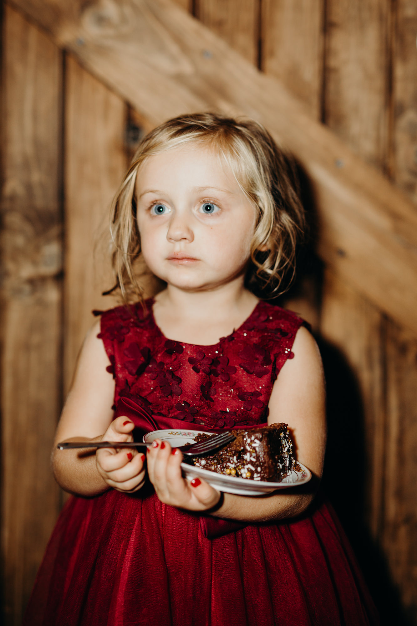 a little girl holds a slice of cake during a wedding reception at hayloft on the arch in syracuse, ny