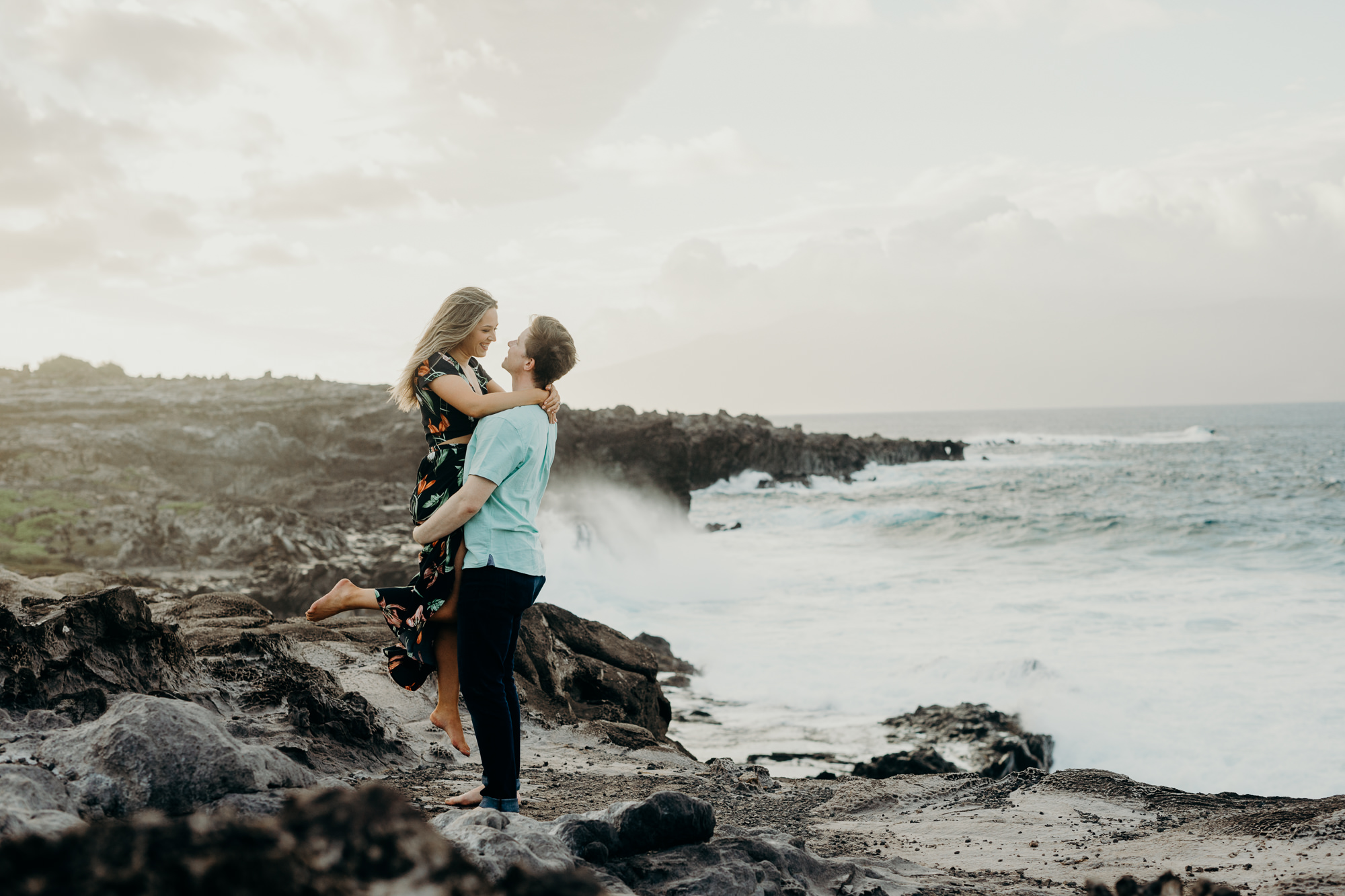 portrait of a couple standing on volcanic rock overlooking the ocean in maui, HI