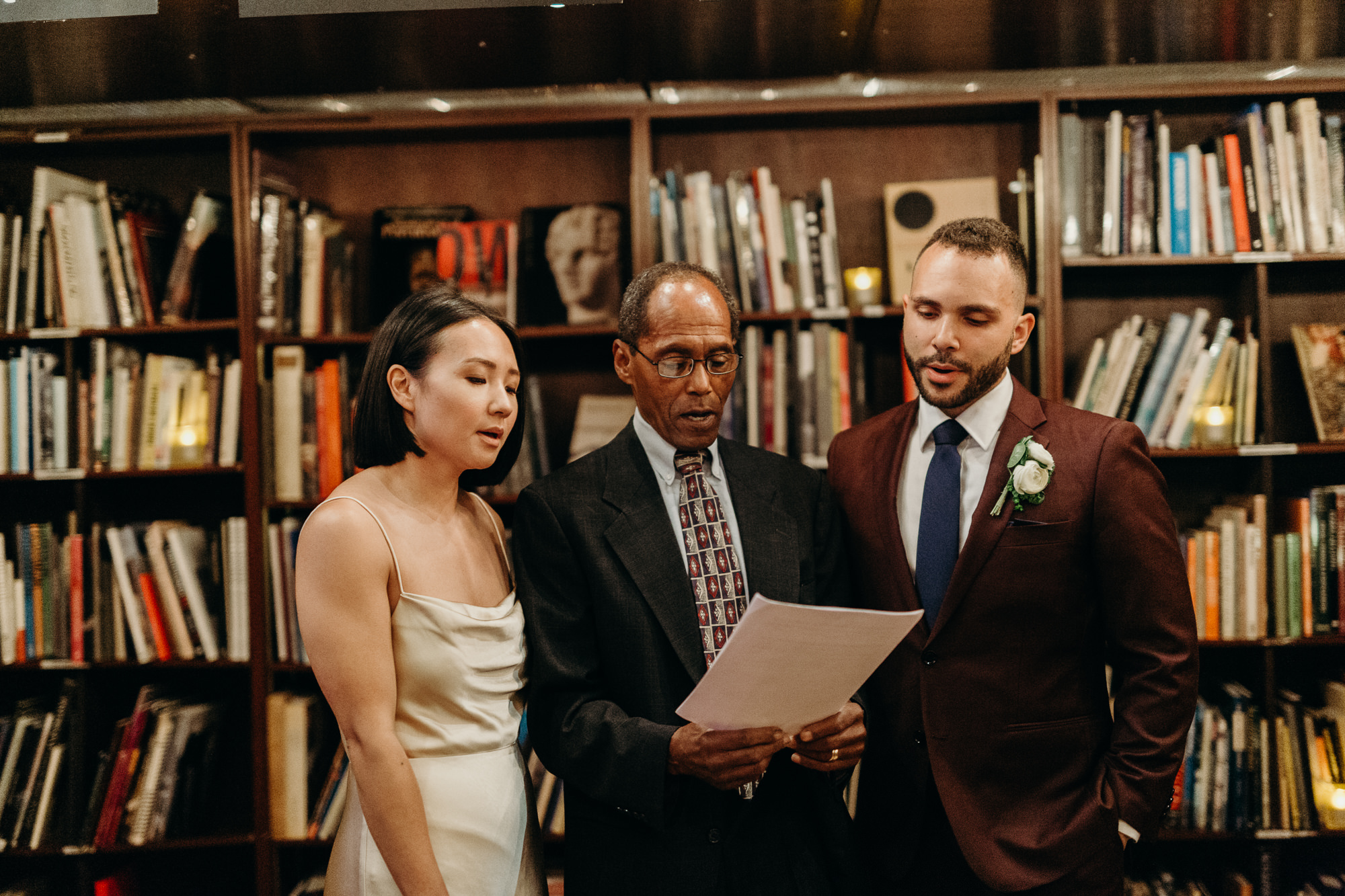 a bride and groom during their wedding ceremony at housingworks bookstore in new york, new york