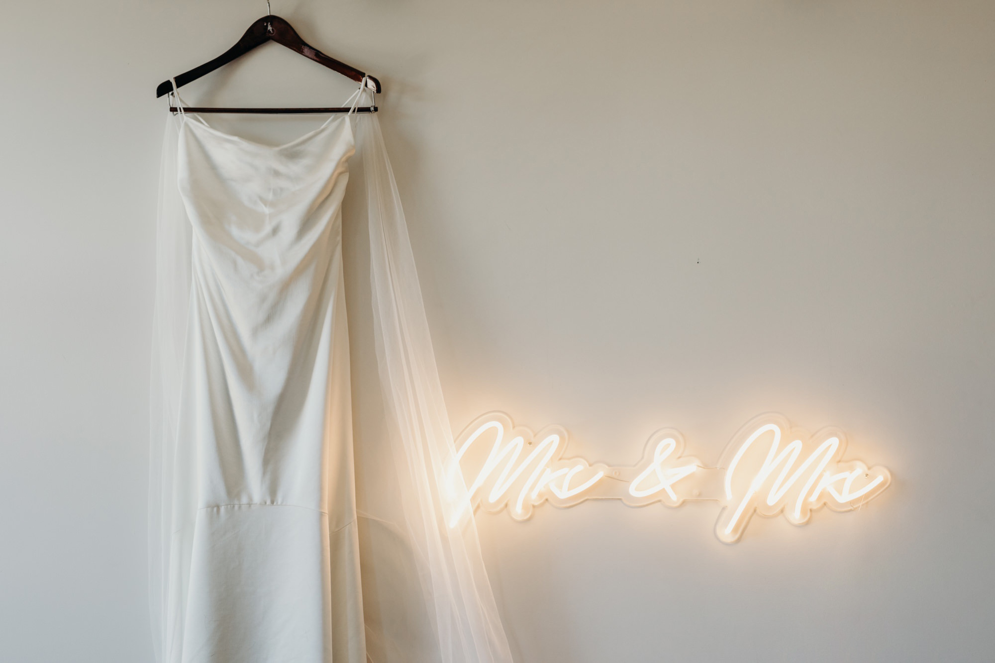 wedding dress hanging next to a neon sign that says mrs and mrs