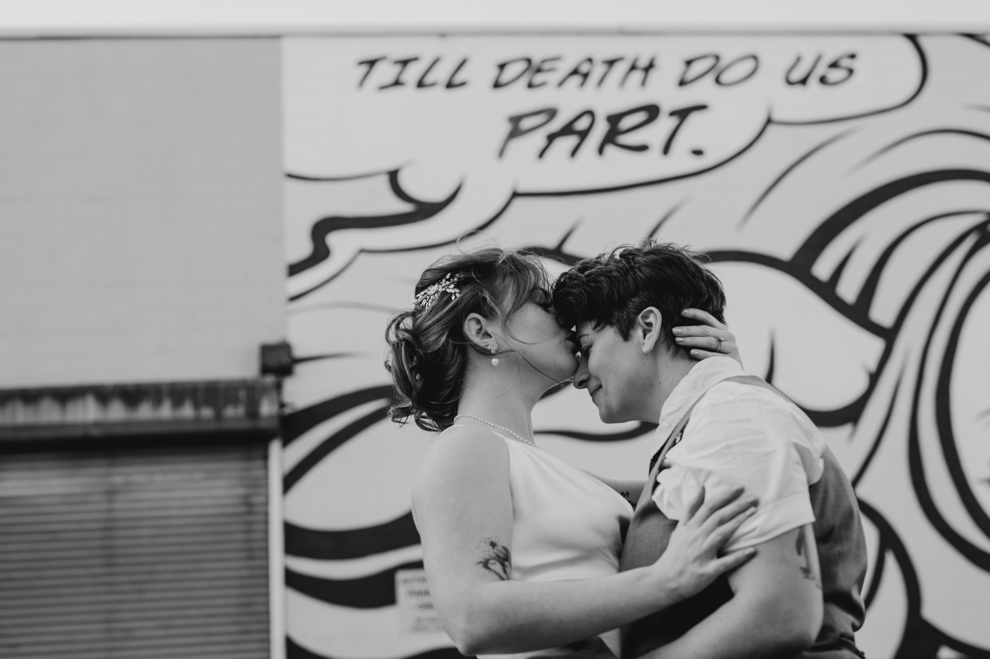 portrait of a couple just married in front of a mural that says til death do us part in bushwick, brooklyn, new york city
