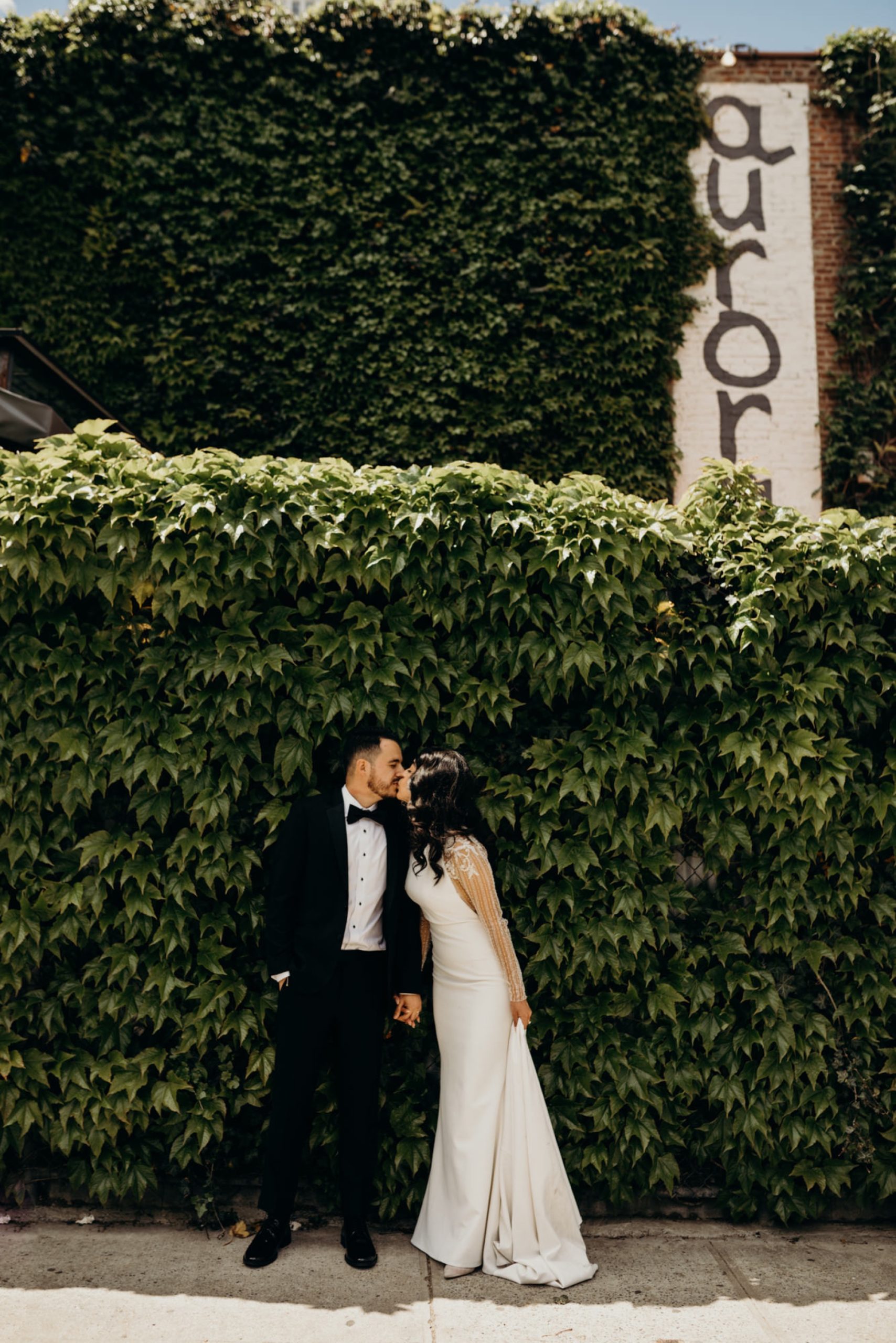 portrait of a bride and groom kissing in front of an ivy wall at aurora brooklyn in new york city