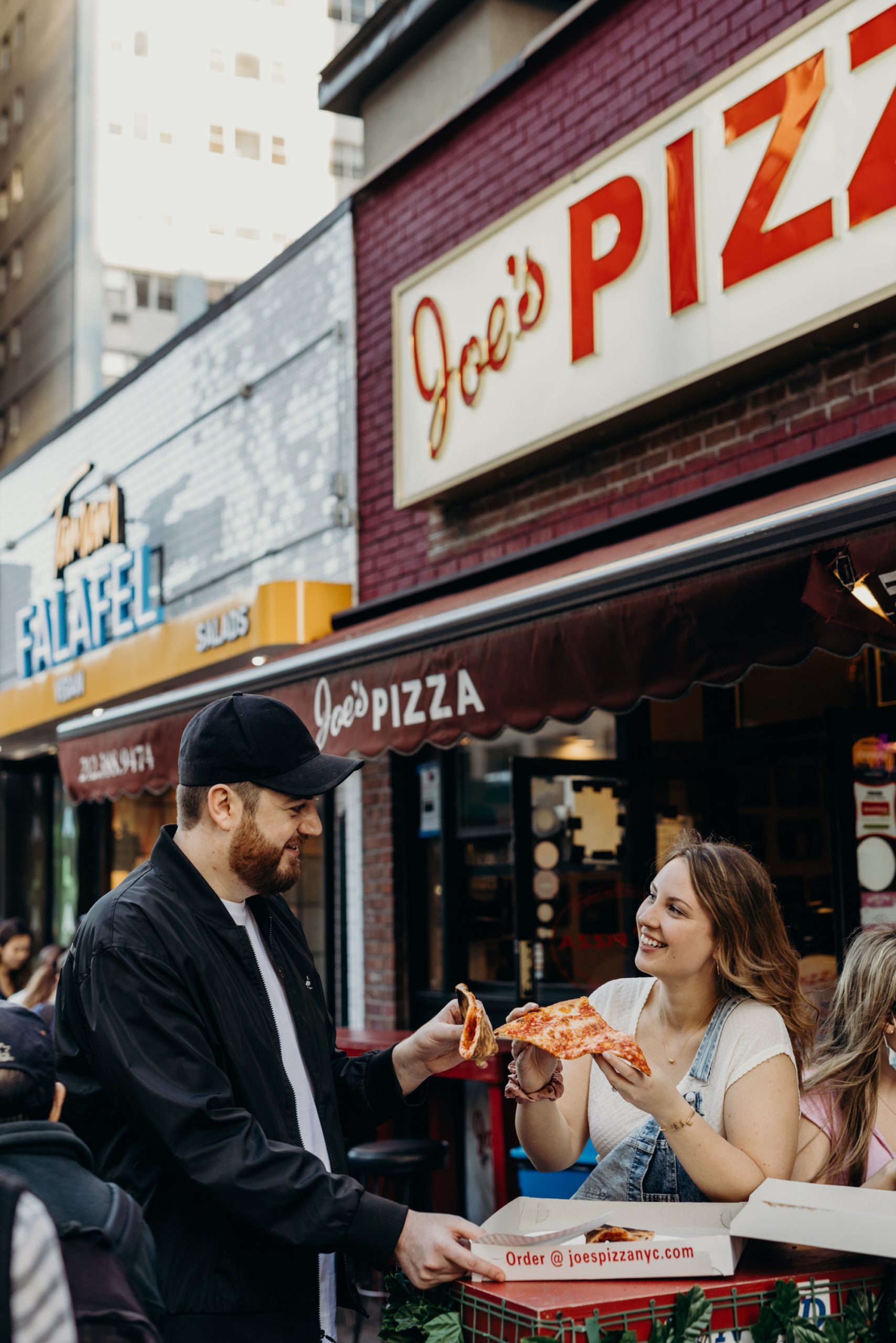 portrait of a couple eating pizza during their engagement session at joe's pizza in new york city