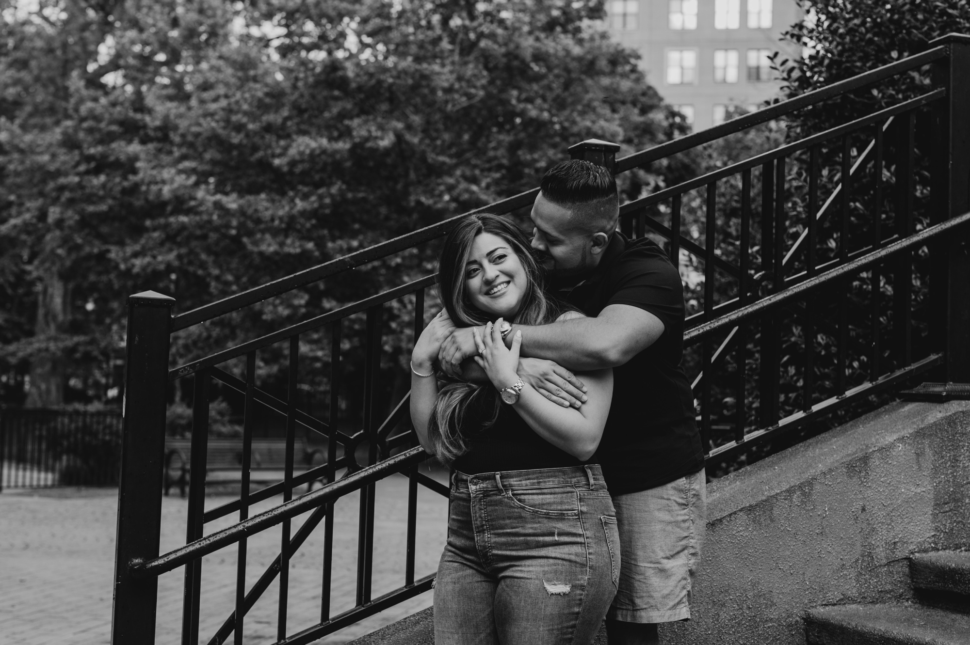 portrait of a couple standing on steps in a park with arms around each other, laughing