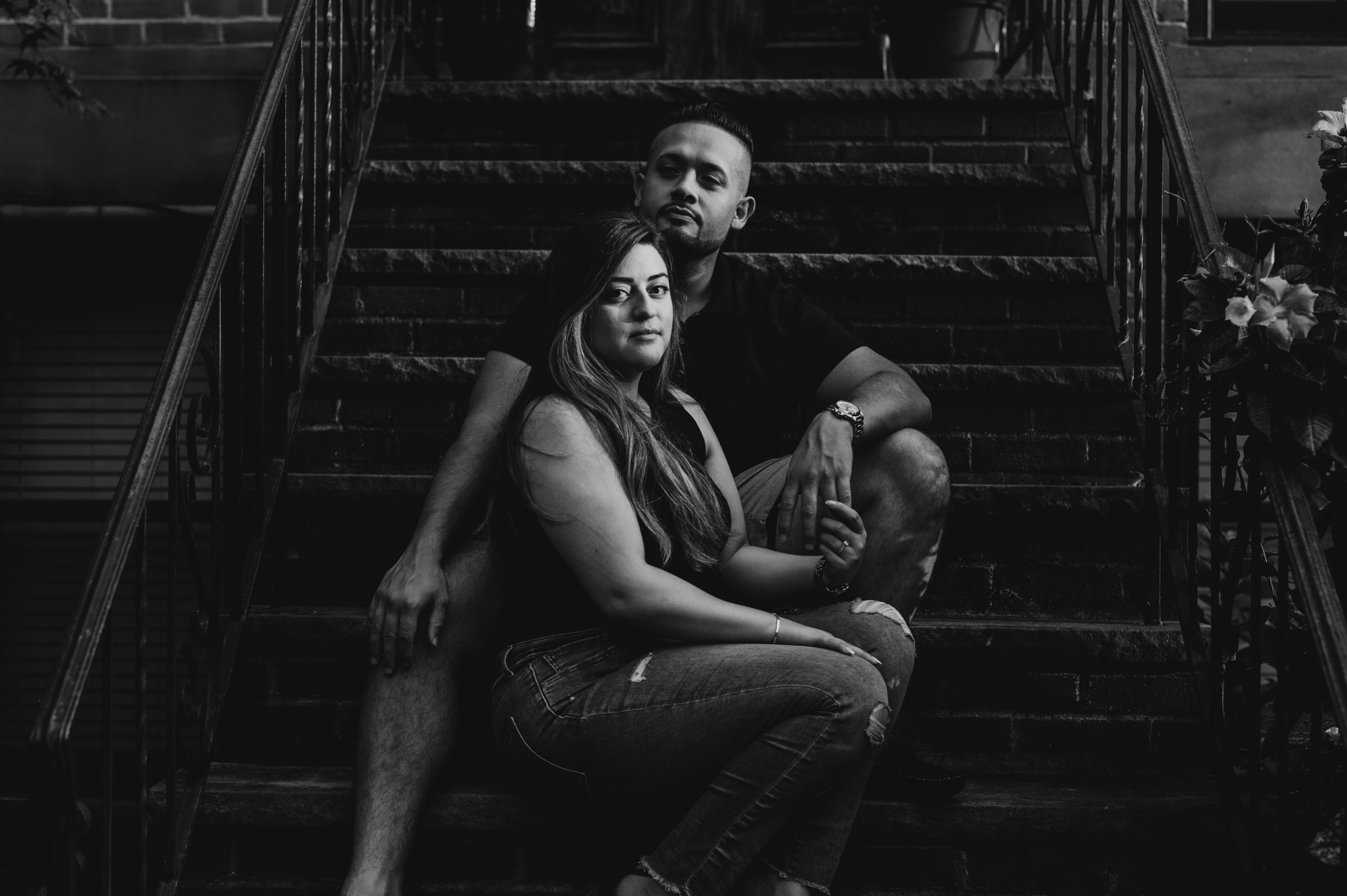 black and white image of a couple sitting on a brownstone stoop, looking at the camera