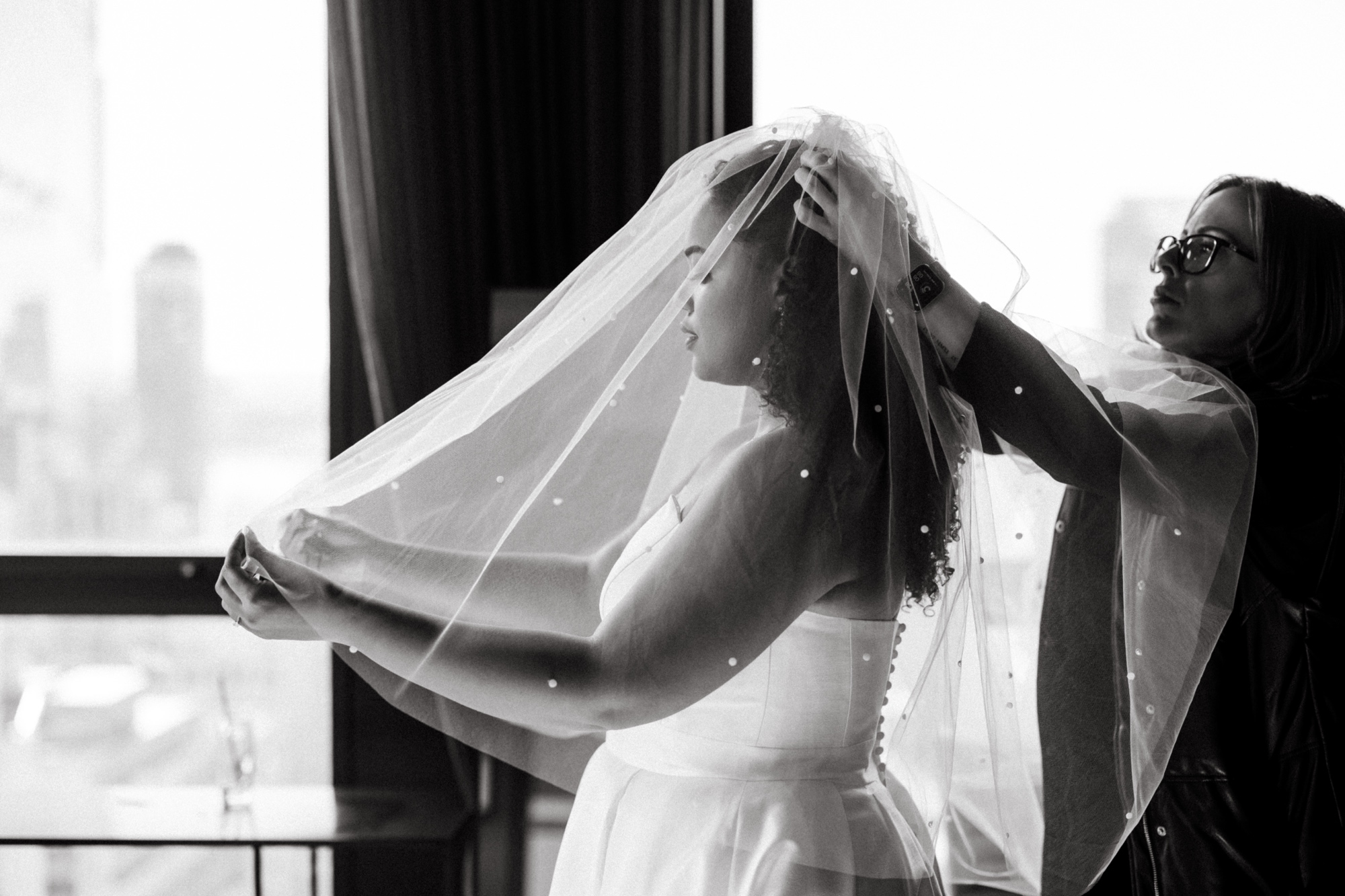 black and white photo of bride putting on her veil