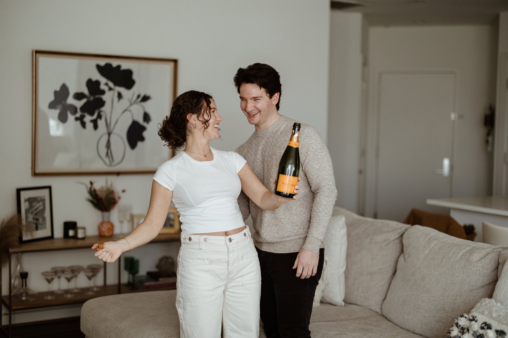 a couple popping a bottle of champagne in their living room