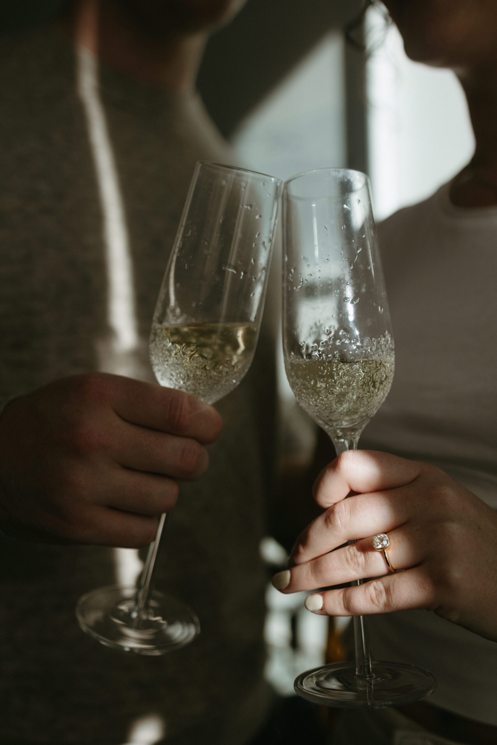 a pair of champagne glasses with an engagement ring highlighted in the sunlight