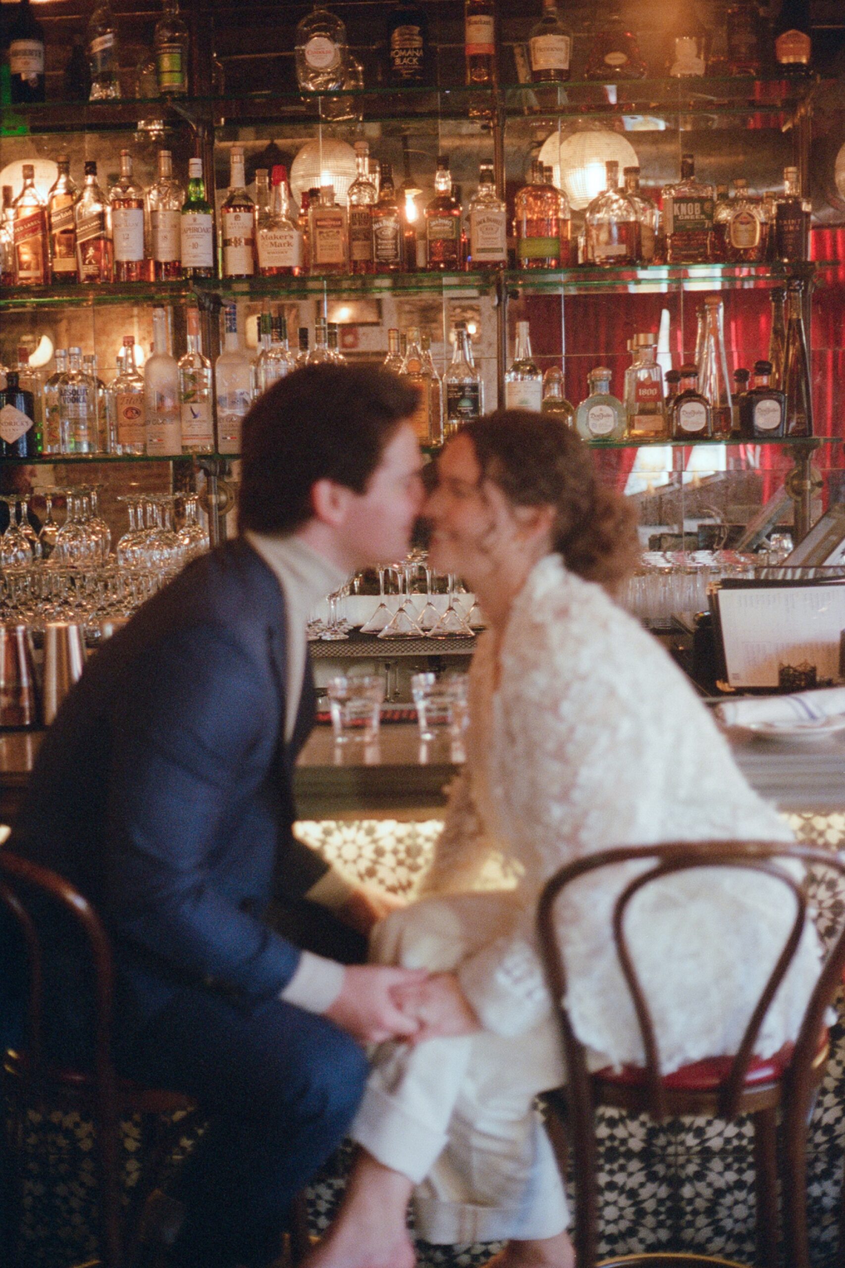 a blurry film photo of a couple sitting at a bar and kissing in hoboken, new jersey