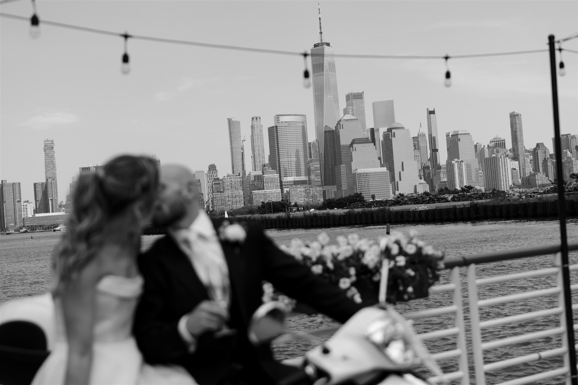 Bride and Groom pose on a vespa on the waterfront deck at Battello, with the manhattan skyline and one world trade center in the background.