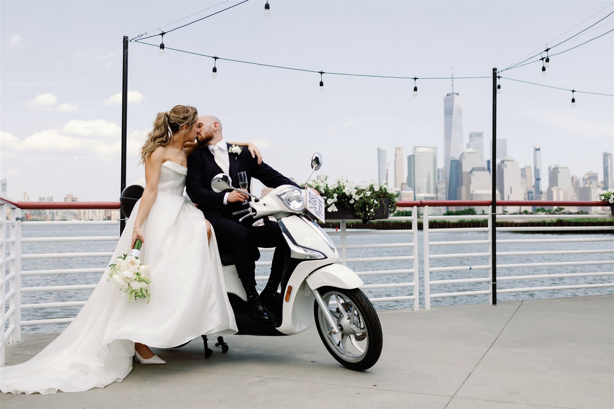 Bride and Groom pose on a vespa on the waterfront deck at Battello, with the manhattan skyline and one world trade center in the background.